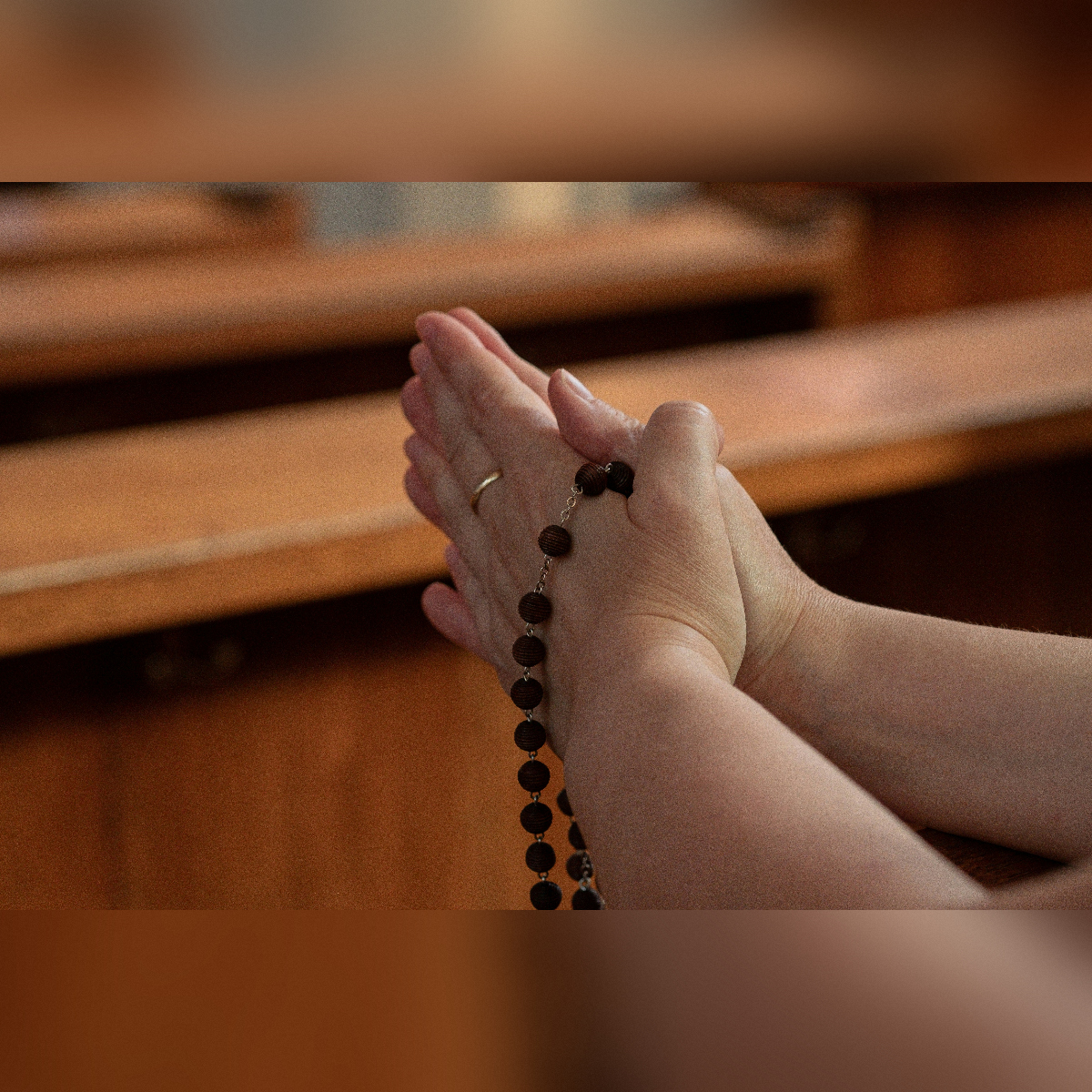 Mani giunte di una donna che tiene un rosario